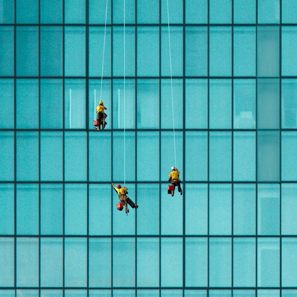 Long shot: Three identically dressed workers clean the regularly-spaced windows of an office block.