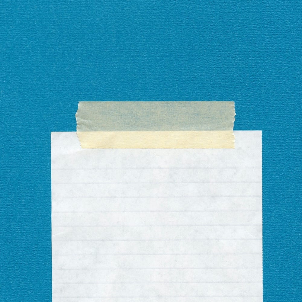 A blank piece of lined paper, stuck to a blue wall with masking tape